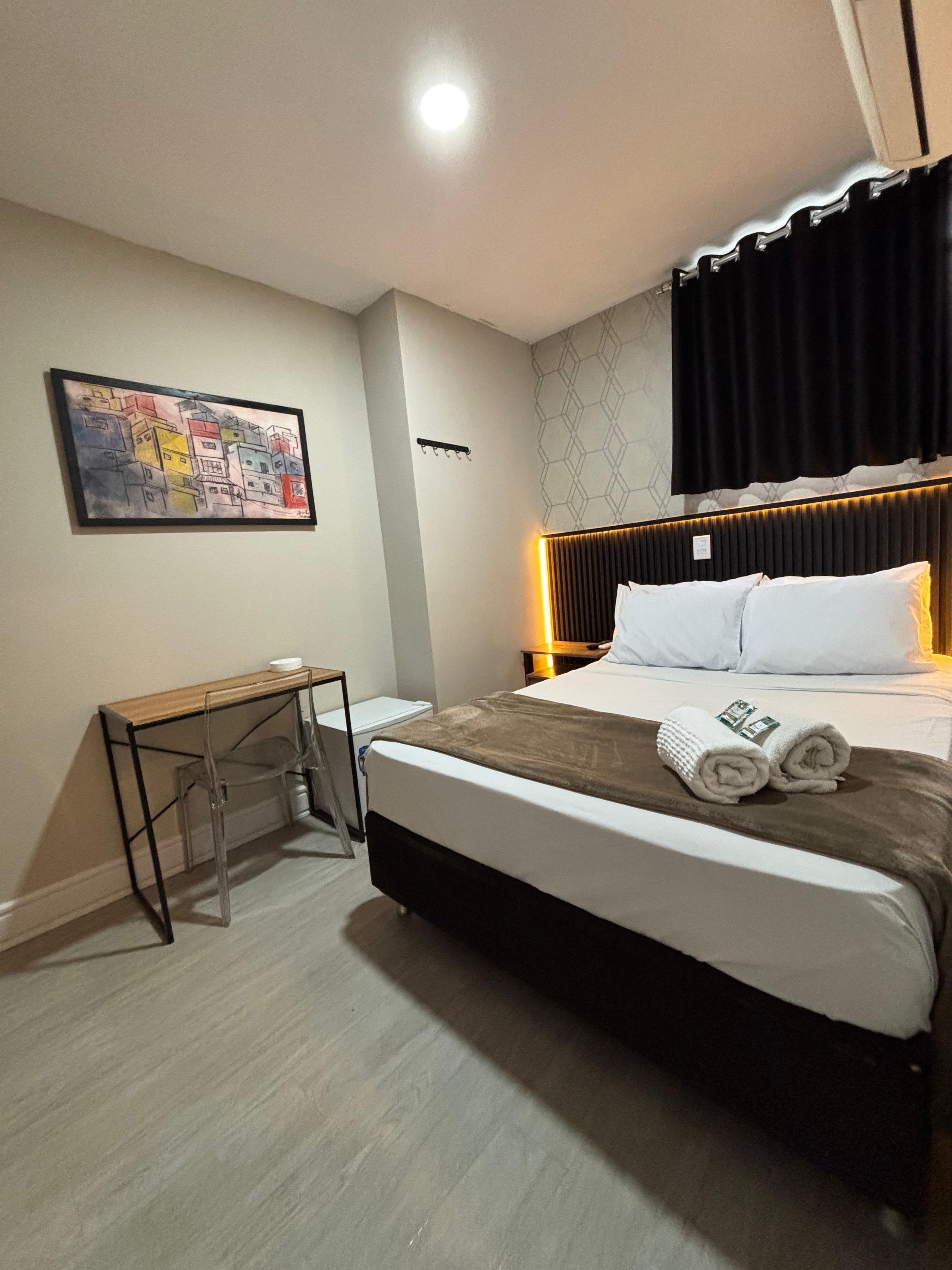 Ein Hotelzimmer mit Bett, Nachttisch, Wandkunst und einem Kopfteil mit integrierter Beleuchtung.