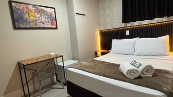Ein Hotelzimmer mit Bett, Nachttisch, Wandkunst und einem Kopfteil mit integrierter Beleuchtung.