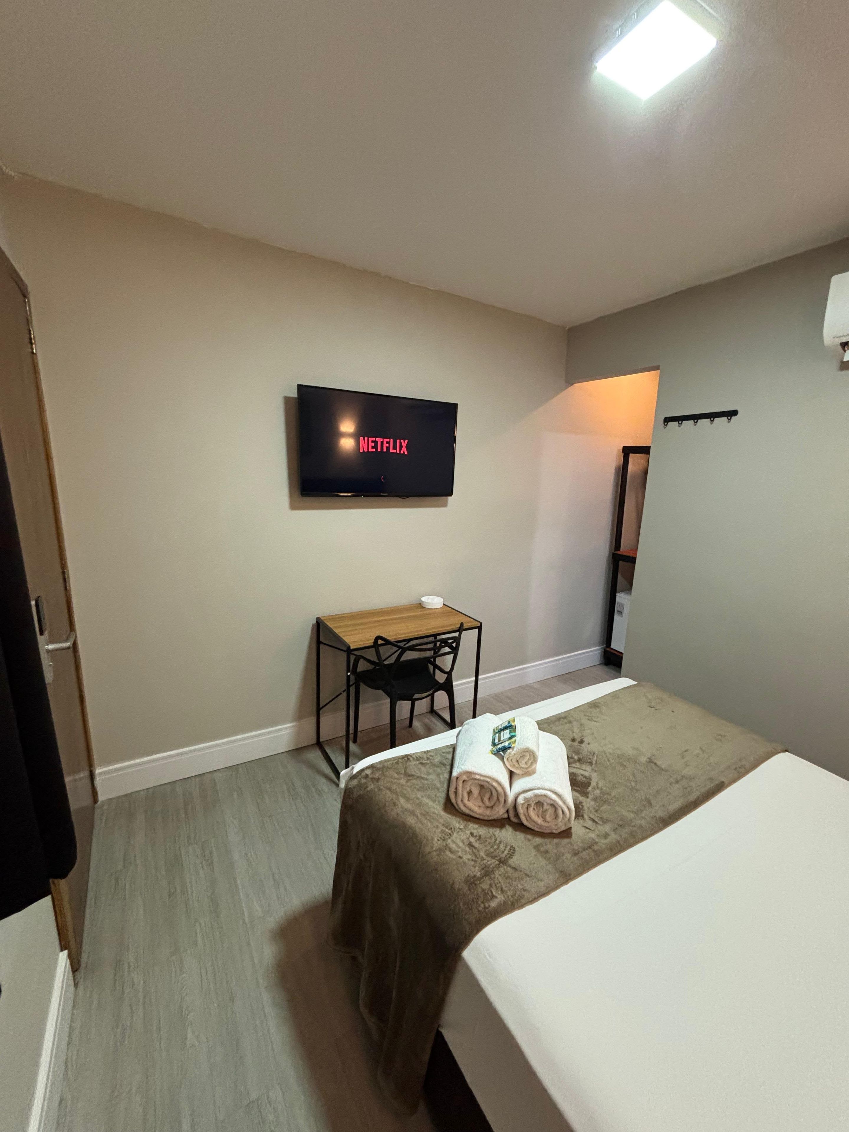 Una habitación de hotel con una cama, un escritorio con una silla, un televisor en la pared y una mesita con un cuenco.
