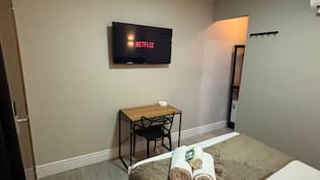 Una habitación de hotel con una cama, un escritorio con una silla, un televisor en la pared y una mesita con un cuenco.