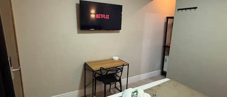 A hotel room with a bed, a desk with a chair, a television mounted on the wall, and a small table with a bowl.