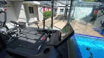 Uma academia em casa com equipamentos de ginástica e vista para uma piscina.