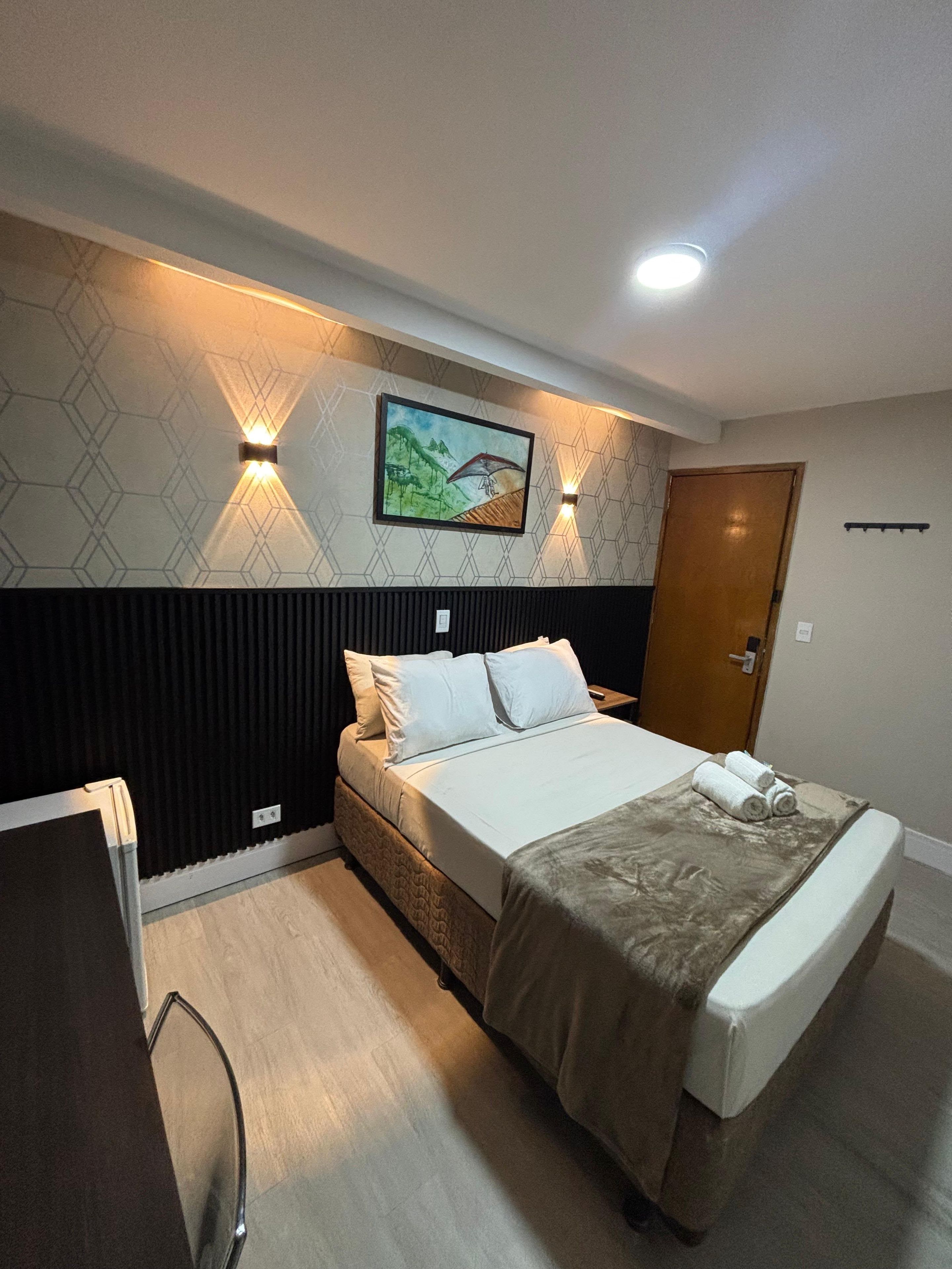 A hotel room with a bed, a painting on the wall, and a door.