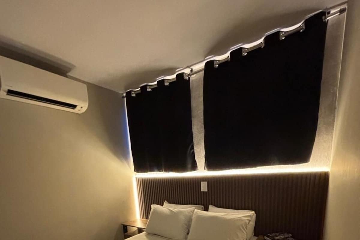 A hotel room with a bed, bedside table, and an air conditioning unit.