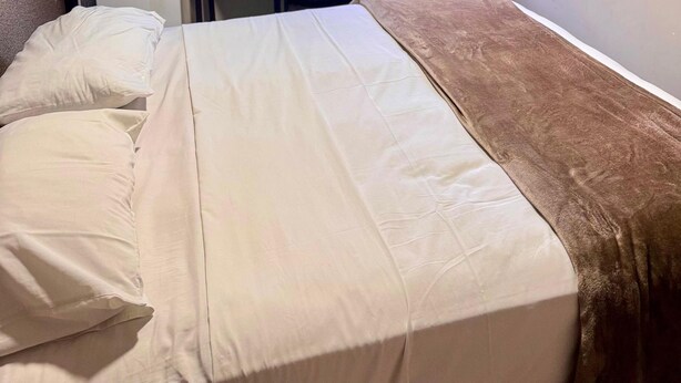 Habitación de hotel con cama, escritorio, silla, televisor y ventana con cortinas.