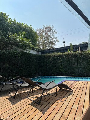 Una terraza de madera con sillas de descanso y una piscina.