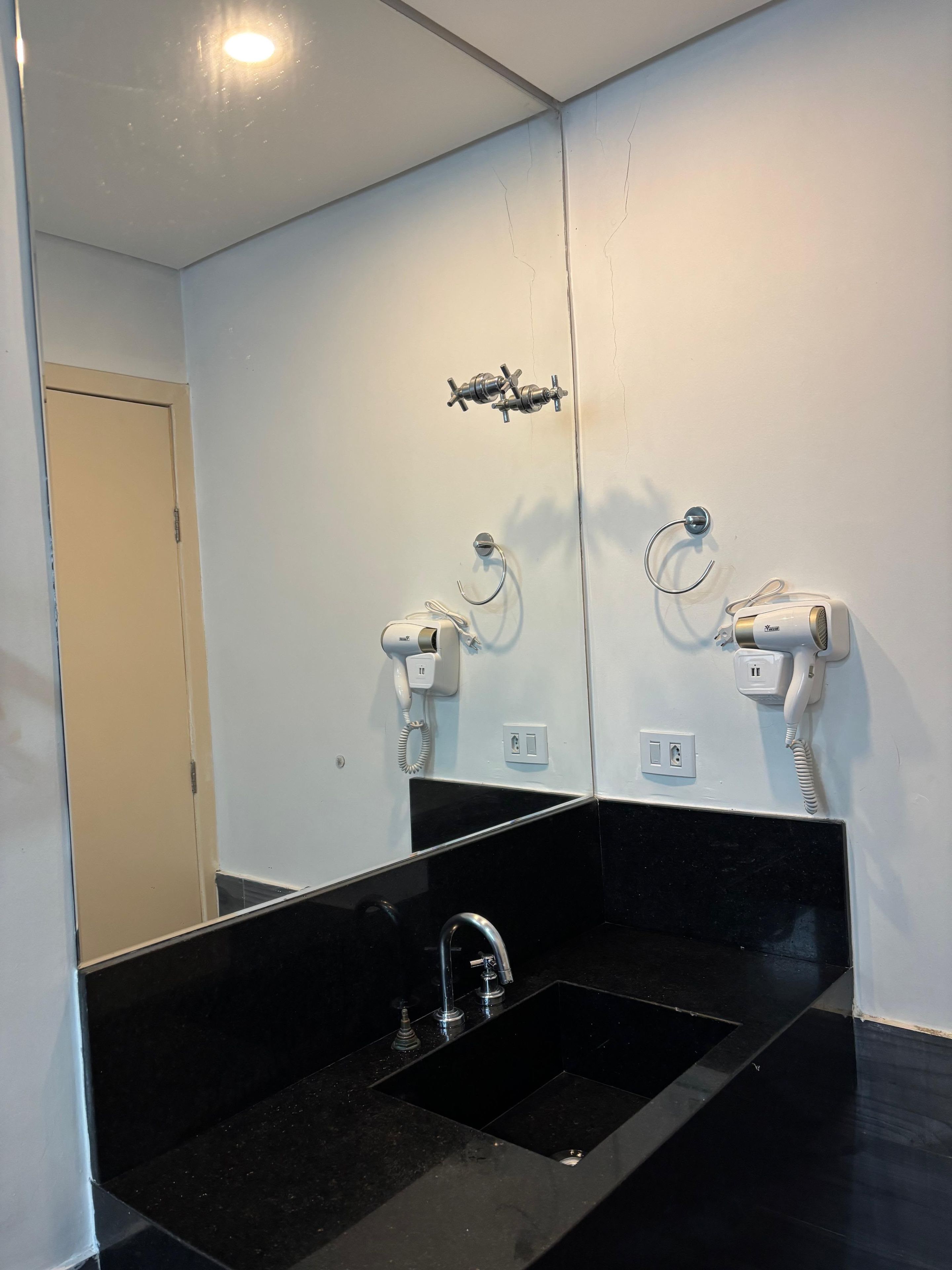 Un baño con un lavabo negro, dos secadores de pelo fijos en la pared y un espejo sobre el lavabo.