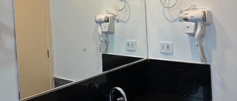 Ein Badezimmer mit einem schwarzen Waschbecken, zwei an der Wand montierten Haartrocknern und einem Spiegel über dem Waschbecken.