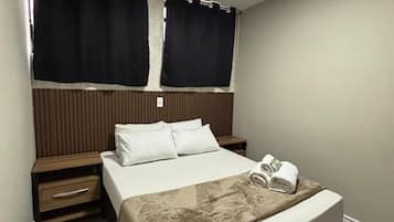 Quarto de hotel com cama, mesas de cabeceira, cortinas e luminária no teto.