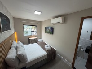 Ein Hotelzimmer mit Bett, Schreibtisch, Stuhl, Fernseher, Klimaanlage und Fenster.