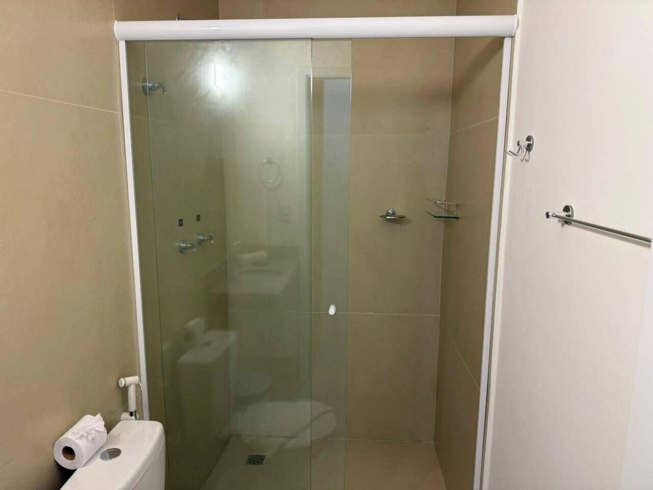 Divisória de chuveiro com paredes de vidro, vaso sanitário e porta-toalhas.