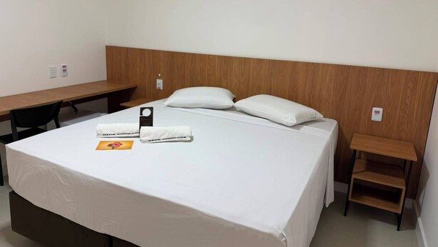 A hotel room with a bed, a desk, and a small wooden side table.