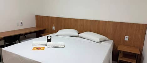 A hotel room with a bed, a desk, and a small wooden side table.