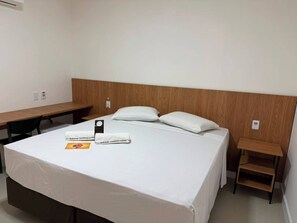 A hotel room with a bed, a desk, and a small wooden side table.