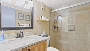 A bathroom with a granite countertop sink, a large mirror, a glass shower enclosure, and a toilet. - Cozy 2 Bedroom Condo in Silverthorne, CO! (Silverthorne)