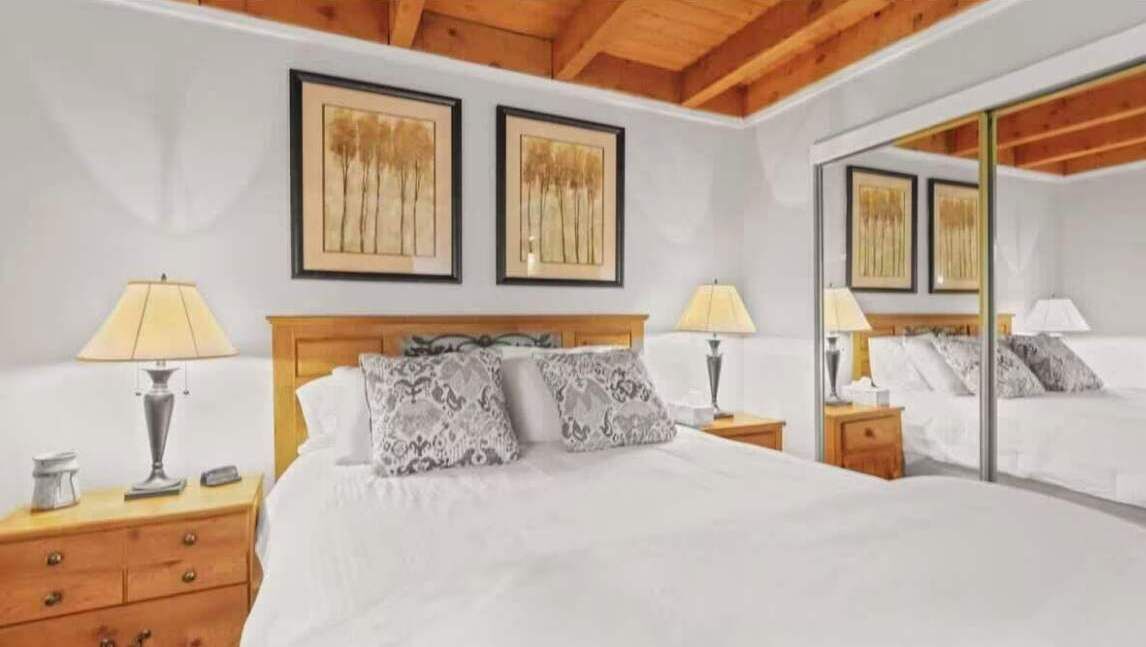 A bedroom with a bed, two bedside tables, lamps, a mirror, and framed artwork on the wall.