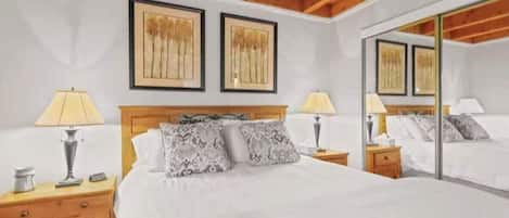 A bedroom with a bed, two bedside tables, lamps, a mirror, and framed artwork on the wall.
