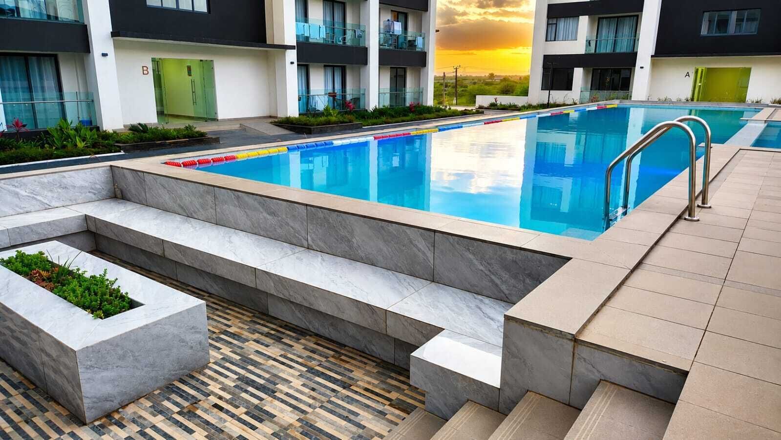 Piscina com degraus de acesso, rodeada por um deck revestido em azulejo e vista para um edifício com varandas.