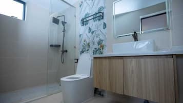 Un baño moderno con cabina de ducha de vidrio, inodoro y tocador con espejo.