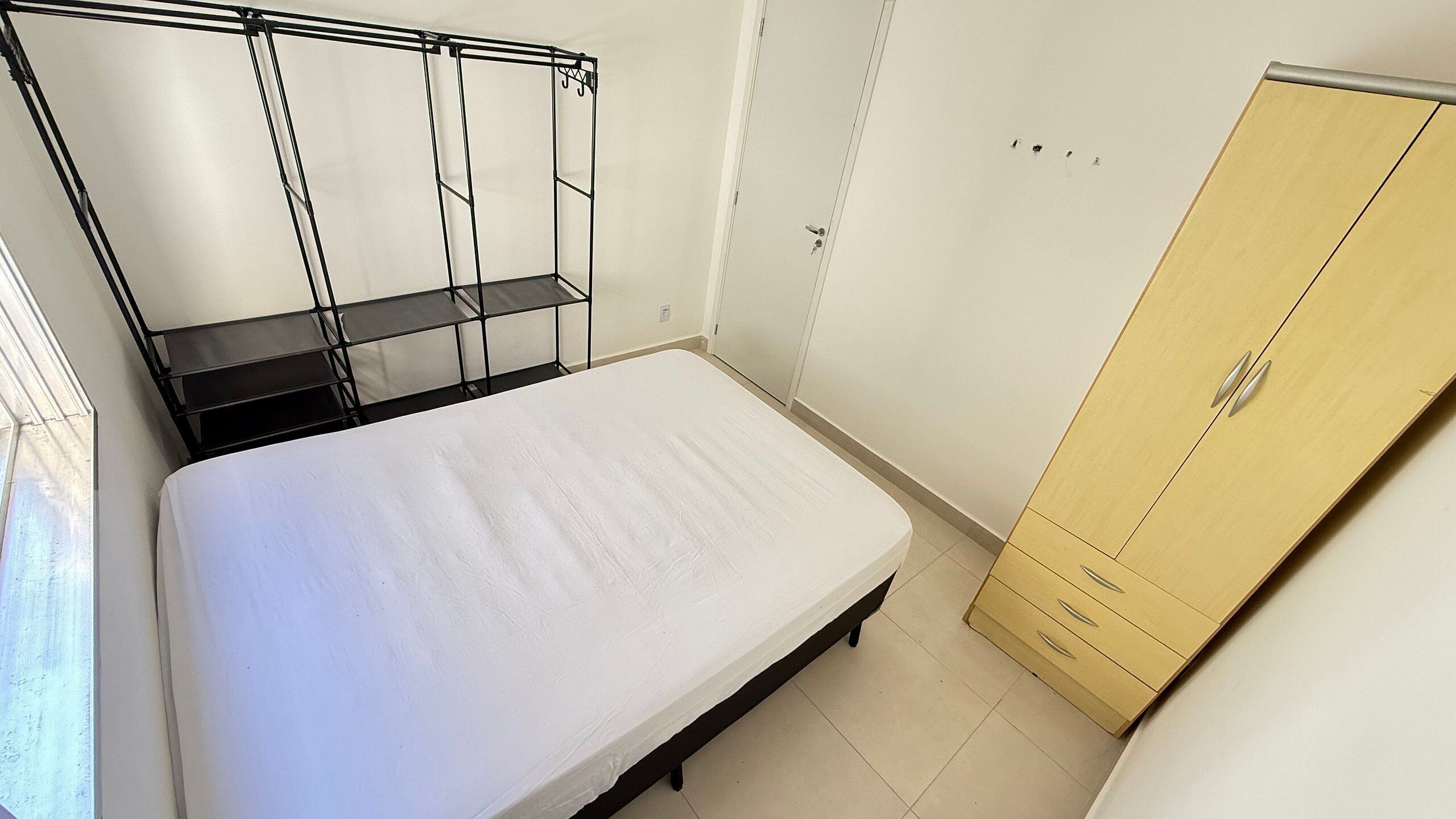 Un dormitorio con cama, armario y estantería metálica.