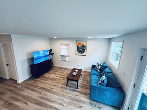 Ein Wohnzimmer mit Flachbildfernseher, einem blauen Sofa, einem Couchtisch und einem Gemälde an der Wand.