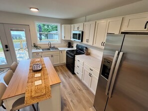 A modern kitchen with white cabinets, a stainless steel refrigerator, a microwave, and a stove.