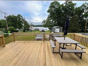 A wooden deck with picnic tables and a covered umbrella, overlooking a residential area with houses and a lake. - Lake My Day – Relaxing Cottage Getaway at Canadohta Lake (Union City)