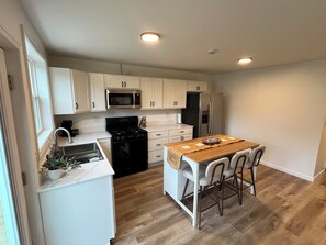 Eine moderne Küche mit weißen Schränken, einer zentralen Kochinsel mit Barhocker, einer Mikrowelle, einem Herd und einem Kühlschrank.
