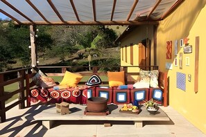 An outdoor seating area with a table, cushions, a small stool, and a pot. - Vida na Roça (São Bento do Sapucaí)