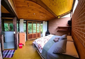 A bedroom with a wooden ceiling, a bed with floral bedding, a brick wall, and a fireplace. - Vida na Roça (São Bento do Sapucaí)