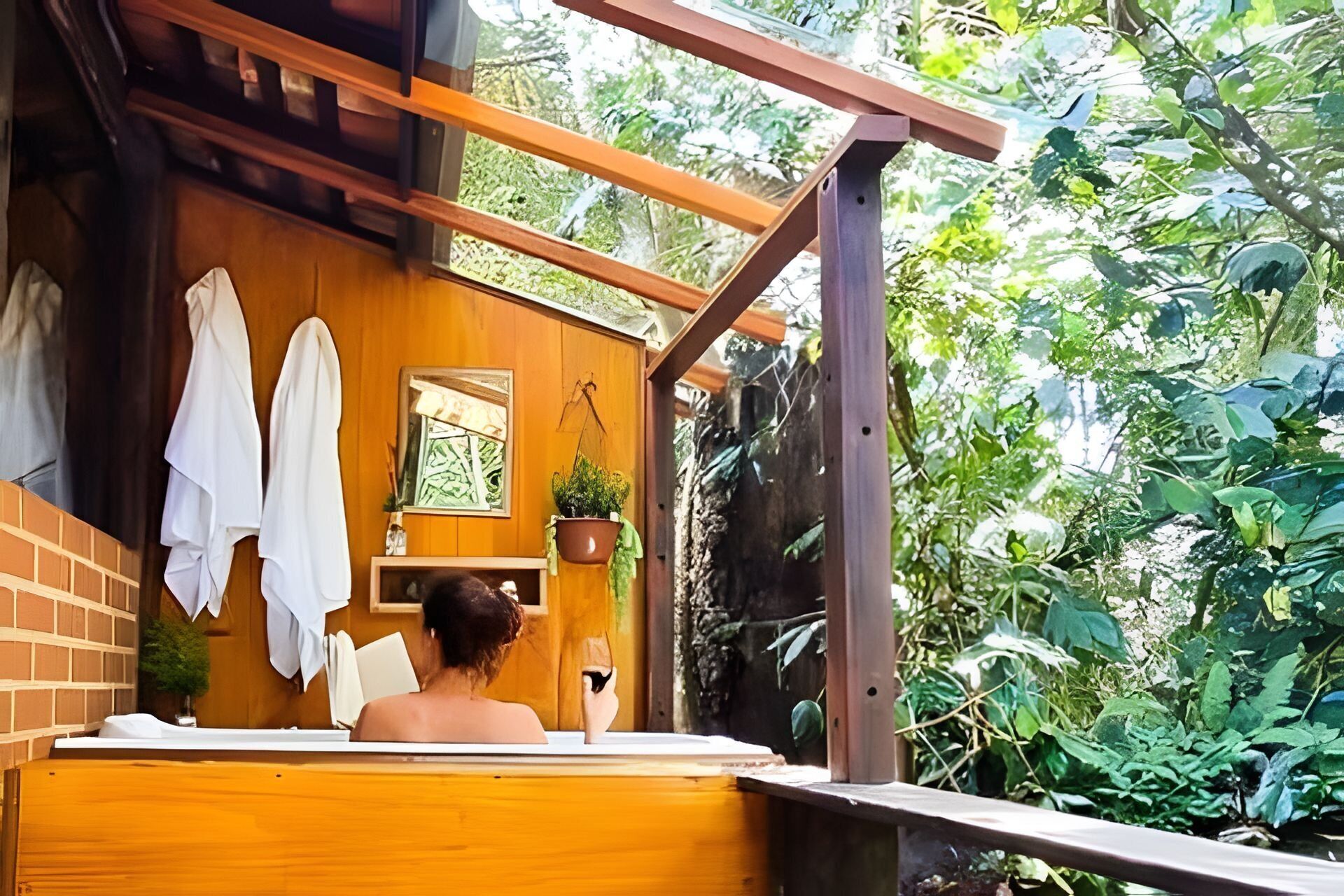 Uma área de spa em madeira com banheira, toalhas e janela com vista para o verde.