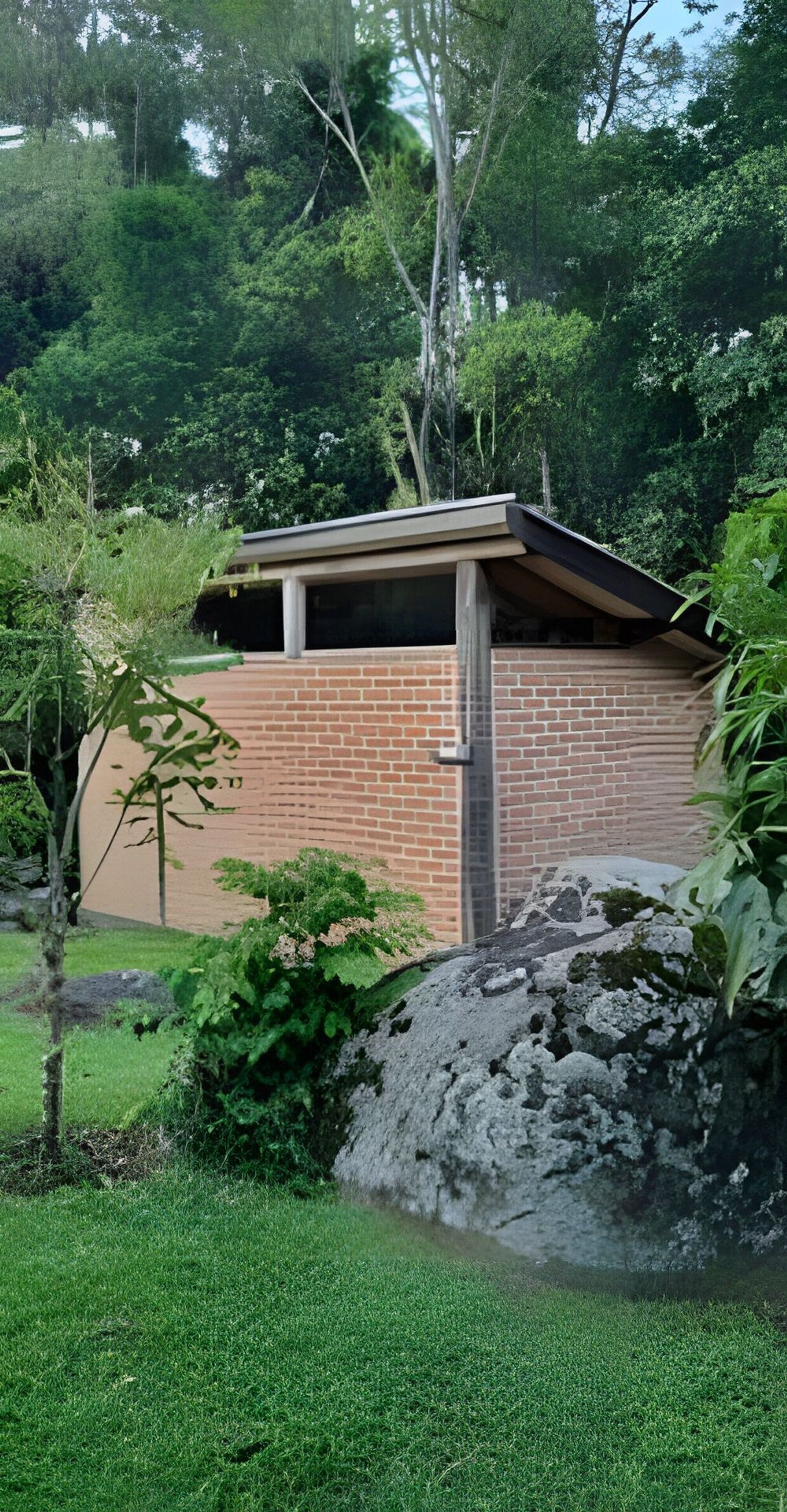 A small brick building with a flat roof, surrounded by lush greenery and a grassy area.