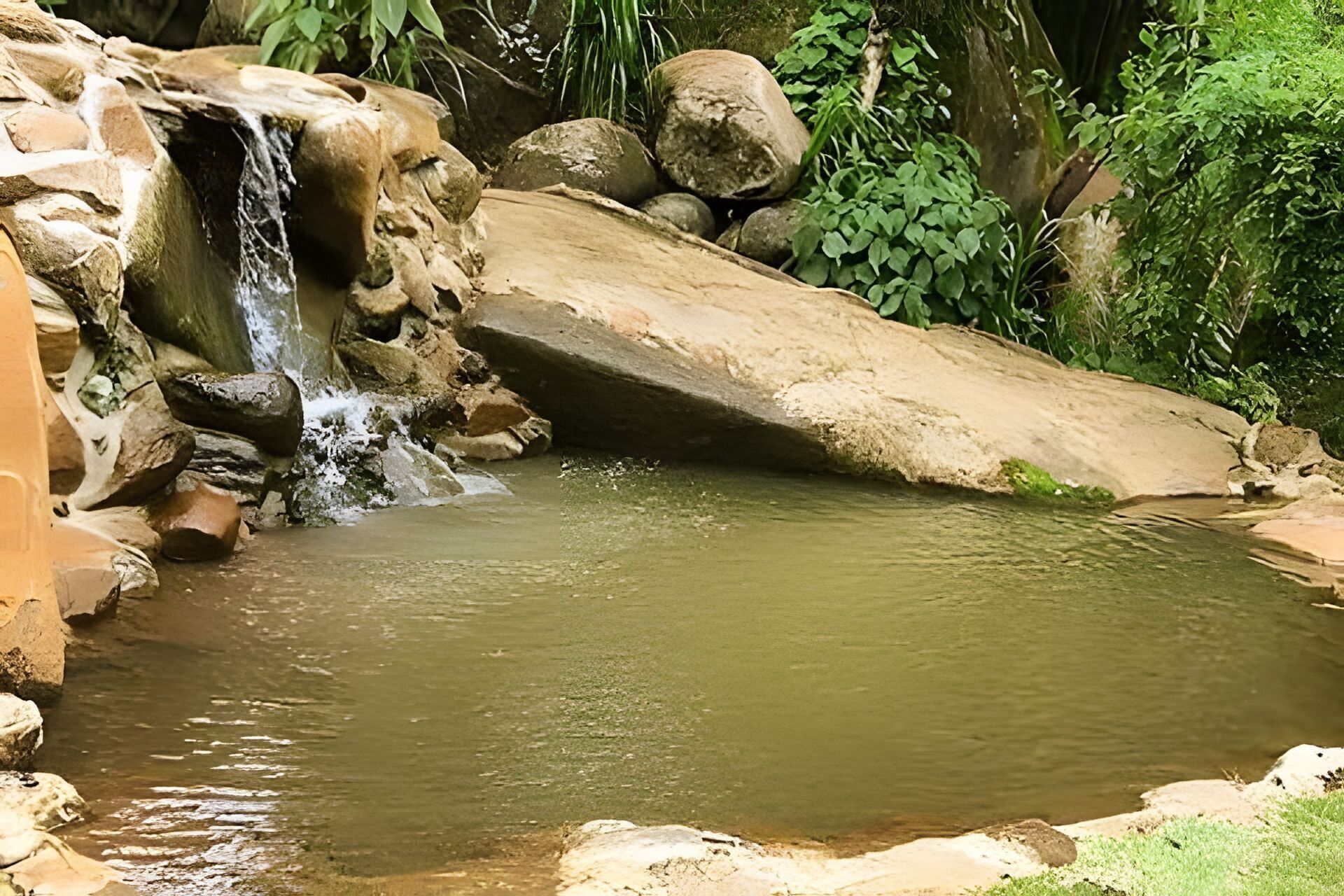 A natural water feature with a small waterfall, surrounded by rocks and greenery.