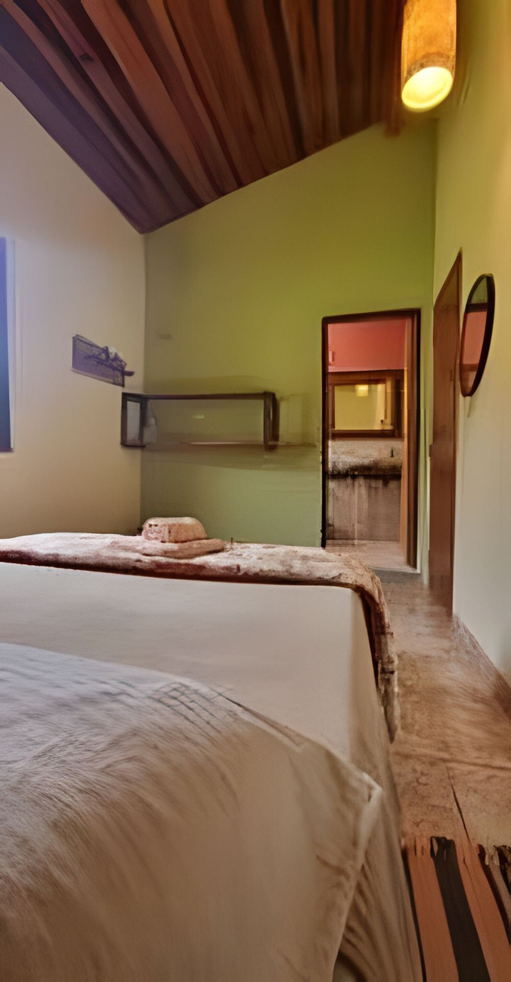 Um quarto com uma cama, um espelho e uma porta que dá para outro cômodo.