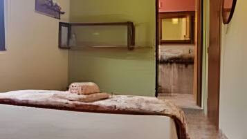 Um quarto com uma cama, um espelho e uma porta que dá para outro cômodo.