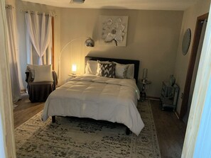 A bedroom with a large bed, a bedside table with a lamp, a wall-mounted flower decoration, and a small side table with a vase. - Spacious 6-bedroom house with AC in soothing POCONO MOUNTAINS (Saylorsburg)