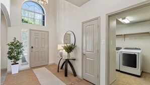 A clean, well-lit entryway with a large mirror, a potted plant, and a door leading to a laundry room. - The Olive House - Stylish 4BR Retreat - Sleeps 10 - Newly Furnished (Tomball)