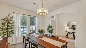 A dining area with a wooden table, chairs, a chandelier, and potted plants. - The Olive House - Stylish 4BR Retreat - Sleeps 10 - Newly Furnished (Tomball)