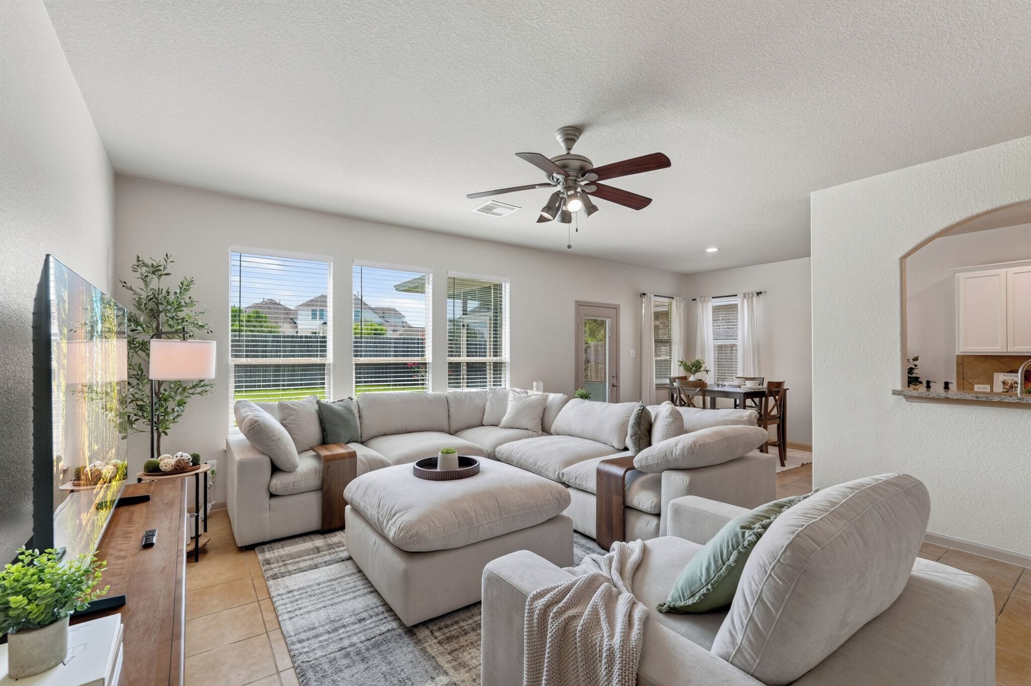 A modern living room with a sectional sofa, a dining area, and a ceiling fan.