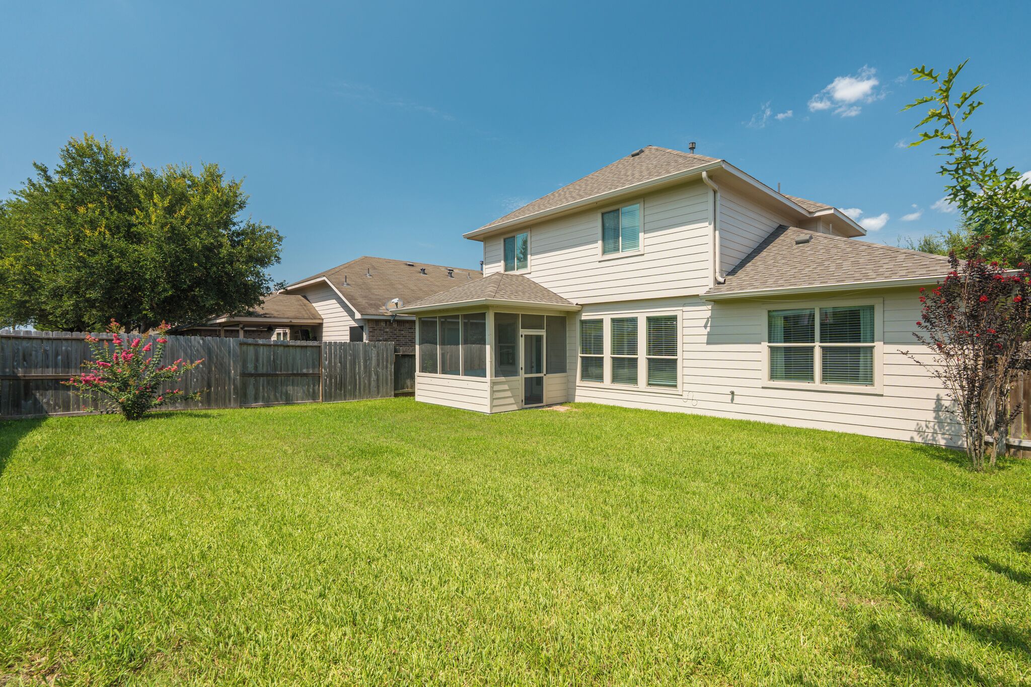 A two-story house with a covered patio, a fenced backyard, and a well-maintained lawn.