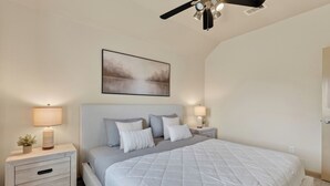 A bedroom with a bed, two bedside tables, a ceiling fan, and a wall-mounted painting. - The Olive House - Stylish 4BR Retreat - Sleeps 10 - Newly Furnished (Tomball)
