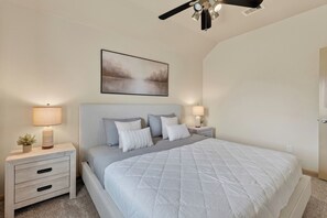 Un dormitorio con una cama, dos mesitas de noche, un ventilador de techo y un cuadro colgado en la pared.