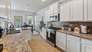 A modern kitchen with white cabinets, a granite countertop, stainless steel appliances, and a view to the outdoors. - The Olive House - Stylish 4BR Retreat - Sleeps 10 - Newly Furnished (Tomball)