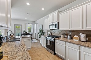 Cocina moderna con armarios blancos, encimera de granito, electrodomésticos de acero inoxidable y vistas al exterior.