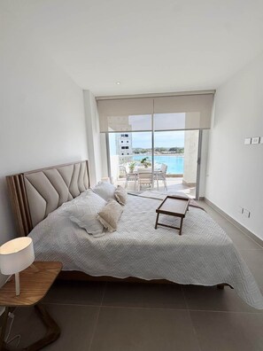 Ein Schlafzimmer mit einem großen Bett, einem Nachttisch und Blick auf einen Pool und eine Sitzgelegenheit im Freien.