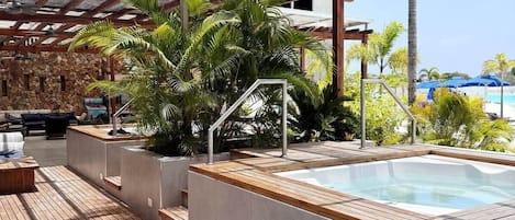 A rooftop pool area with a hot tub, wooden deck, and outdoor seating.