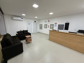 Una zona de recepción con un escritorio de madera, sofás negros, una mesita y un equipo de aire acondicionado blanco en la pared.