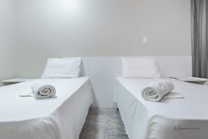 A hotel room with two single beds, each with a rolled white towel. The room has white bedding and a marble floor. - Rede Andrade Renascença (São Luís)