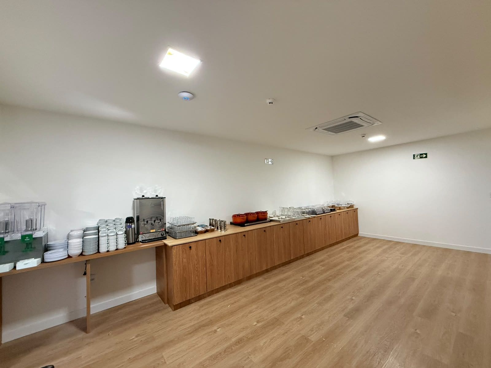 Una habitación amplia con una larga barra de madera, una cafetera y diferentes vasos.