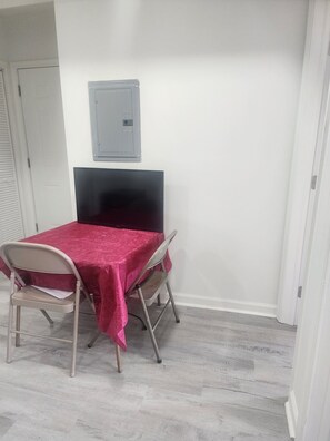 A room with a table covered in a red tablecloth, two chairs, a black TV on a stand, and a white door. - Fantastic 2-bedroom apartment with AC in Drexel Hill (Drexel Hill)